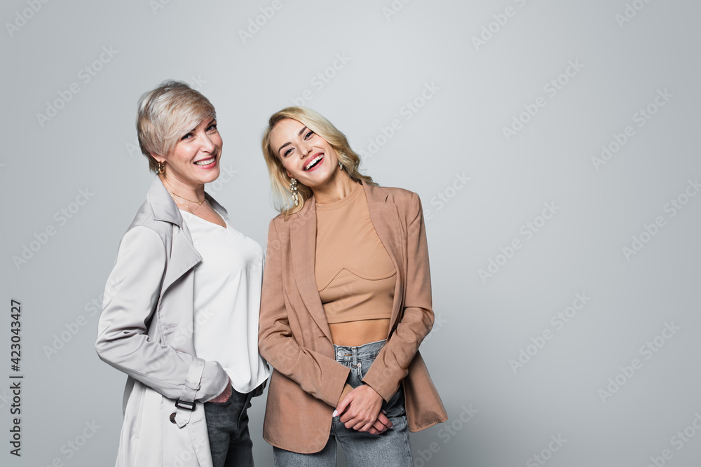 joyful, stylish mother and daughter smiling at camera isolated on grey joyful, stylish mother and daughter smiling at camera isolated on grey