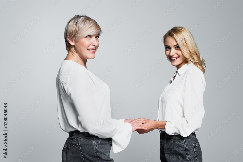 cheerful mother and daughter in white blouses holding hands isolated on grey cheerful mother and daughter in white blouses holding hands isolated on grey