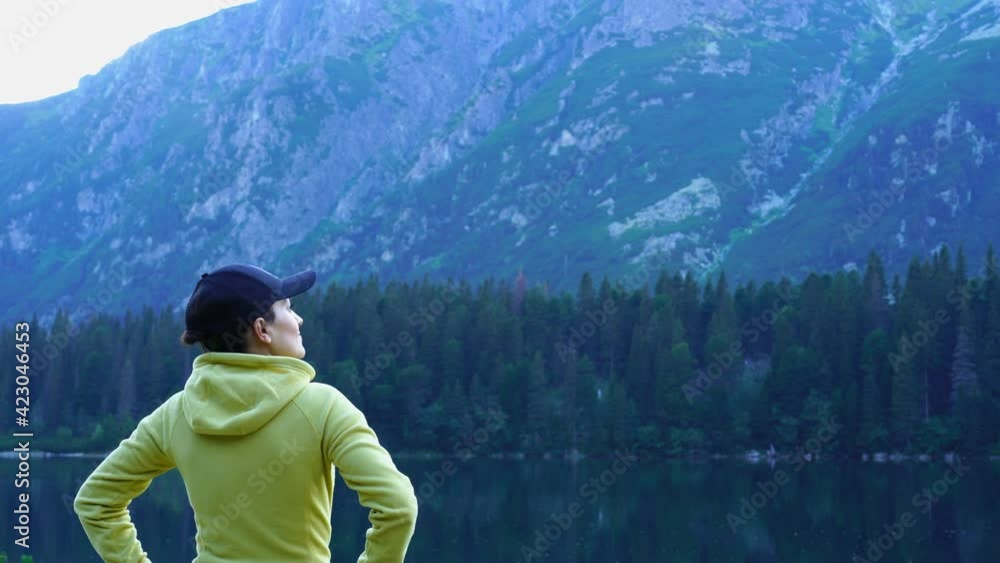 Young female tourist standing by the lake enjoying beautiful view in the mountains, Popradske mountain lake, Slovakia, High Tatras Young female tourist standing by the lake enjoying beautiful view in the mountains, Popradske mountain lake, Slovakia, High Tatras