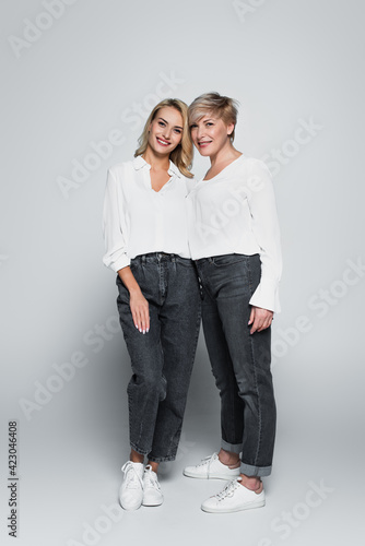 full length view of stylish mother and daughter looking at camera while posing on grey