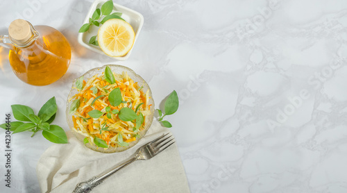 Cabbage, grated carrot and pumpkin salad with oil, basil and rosemary on a marble background with copy space, flat lay