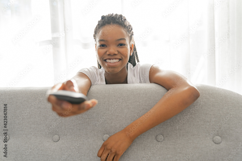 Φωτογραφία Young African American teen on a sofa in her living room relaxing watching tv