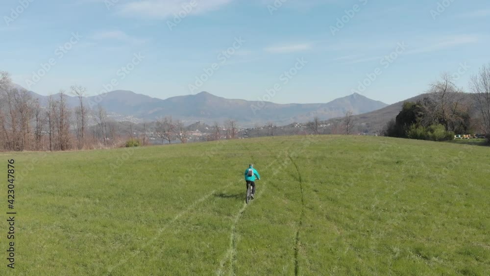 Aerial: man having fun by riding mountain bike in the grass on sunny day, scenic alpine landscape, fitness wellbeing sport in nature, native flat color profile Aerial: man having fun by riding mountain bike in the grass on sunny day, scenic alpine landscape, fitness wellbeing sport in nature, native flat color profile