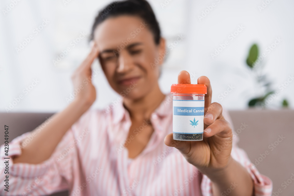 blurred african american woman suffering from migraine and holding bottle with medical cannabis blurred african american woman suffering from migraine and holding bottle with medical cannabis