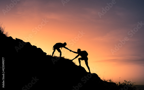 Silhouette of two hikers climbing to the top of a mountain.Teamwork, and giving. helping hand concept. 
