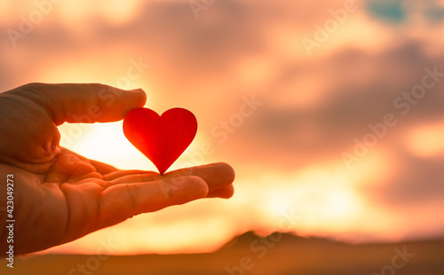 Hand holding heart against sunset background. 