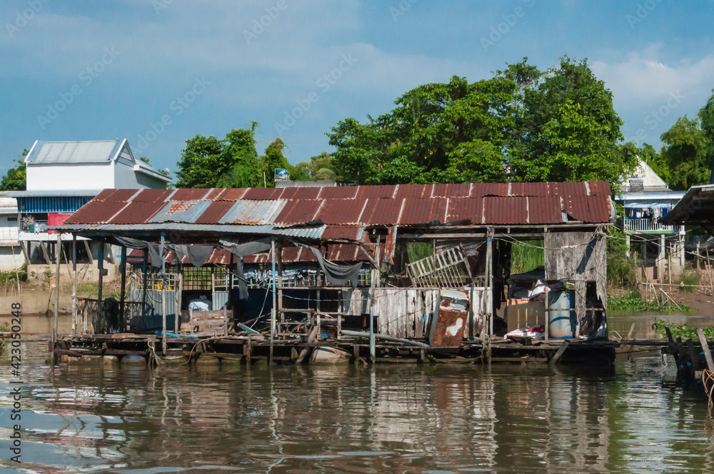 Blick vom Mekong auf den Uferbereich. Dieser ist gesäumt mit typischen Stelzenbauten, gebaut aus Wellblech.   