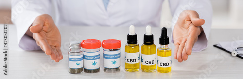cropped view of african american doctor pointing with hands at bottles with medical cannabis and cbd, banner