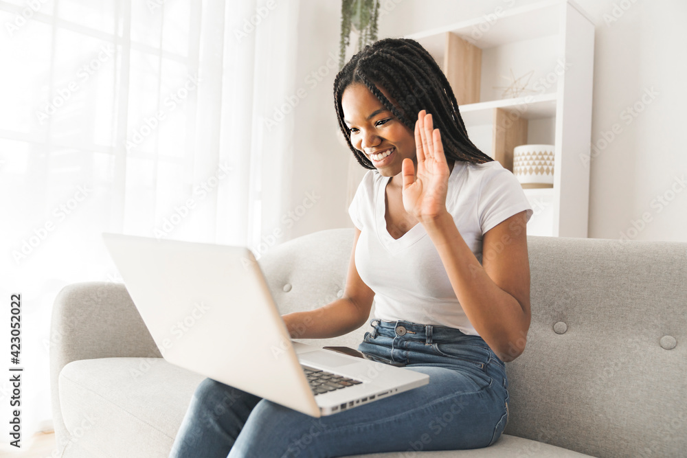 Young African American teen on a sofa in her living room talking with someone on laptop Young African American teen on a sofa in her living room talking with someone on laptop