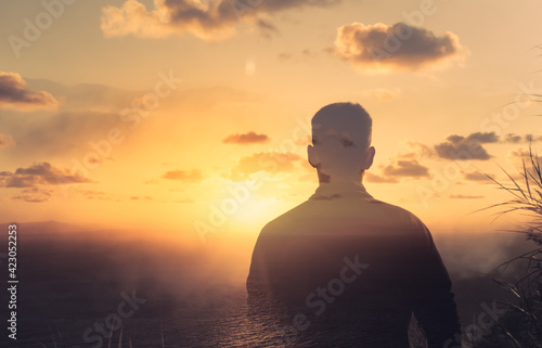 Young thoughtful man on a mountain facing the sunrise. Life vision, and mental health concept. 