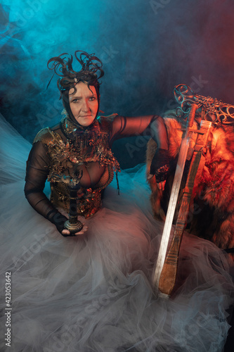 Fabulous creature, queen, sorceress, in a colorful suit and sword. Woman, model after 60, in the studio, dark background