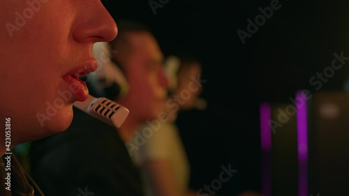 Lips of a man speaking into a microphone while playing a video game. It is illuminated by a monitor with overflowing colors. He plays with his team that sits next to. High quality 4k footage