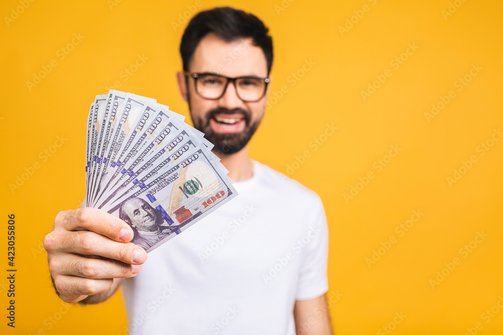 Happy winner! Young rich man in casual holding money dollar bills with surprise isolated over yellow background. Happy winner! Young rich man in casual holding money dollar bills with surprise isolated over yellow background.