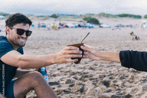 Young man sharing yerba mate with a girl at the beach.