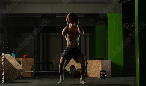 Fit man throwing medicine ball doing ball slam against gym floor or shoulder press exercise..