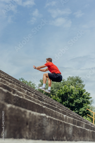 Side view picture of an active male athlete jumping up on stairs in outdoor training. .