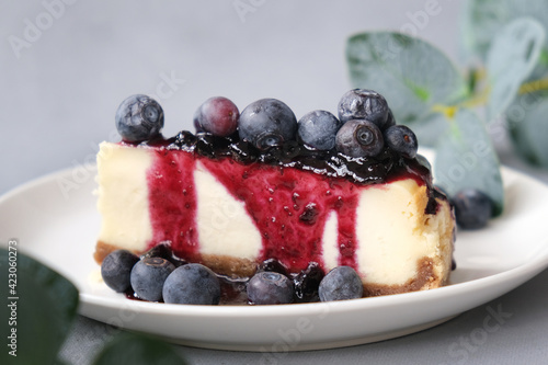 Sweet cheese pie poured jam and decorated fresh blueberries. Slice of tasty cheesecake on plate.