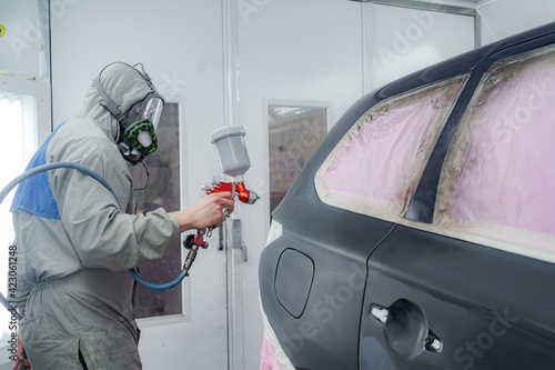 Side view of male in respiratory mask and protective suit painting car with spray gun in service