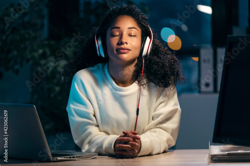 Confident african woman listening to music with earphones while relaxing of work in the office at home.