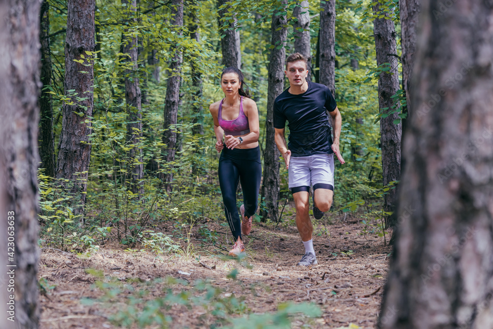 Young athletic couple is running outdoors in the wooded forest area