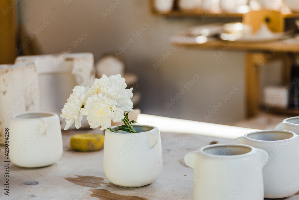 Set of white ceramic cups with flowers placed on counter in light studio near objects for handicraft