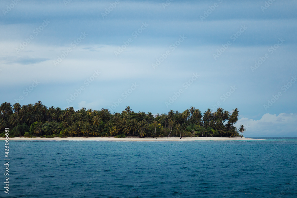 Picturesque view of idyllic island with tropical green trees on sandy beach surrounded by blue sea against clear sky in Indonesia Picturesque view of idyllic island with tropical green trees on sandy beach surrounded by blue sea against clear sky in Indonesia