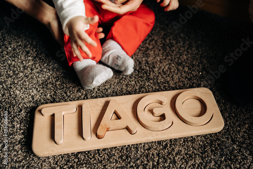 Cropped unrecognizable little baby playing on floor with wooden toy with Tiago name letters