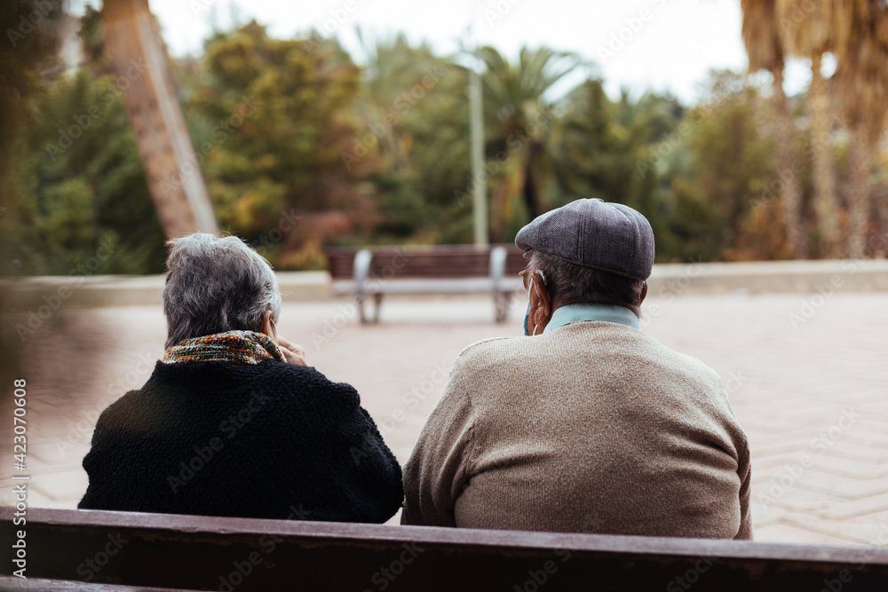 Back view of an unrecognizable elderly couple sitting on a park bench ...
