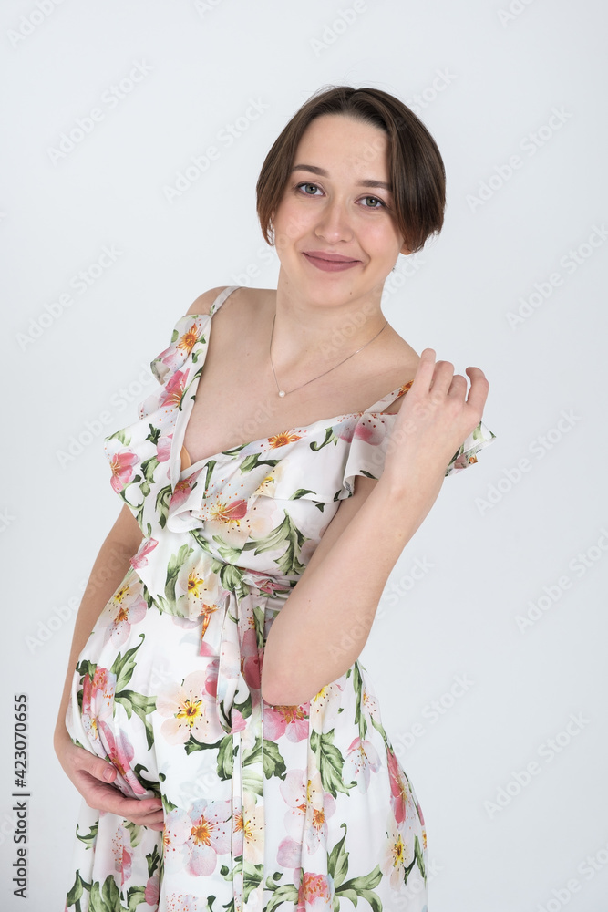 Studio portrait of cheerful young pregnant woman in summer dress on white gray background, happy pregnancy concept Studio portrait of cheerful young pregnant woman in summer dress on white gray background, happy pregnancy concept