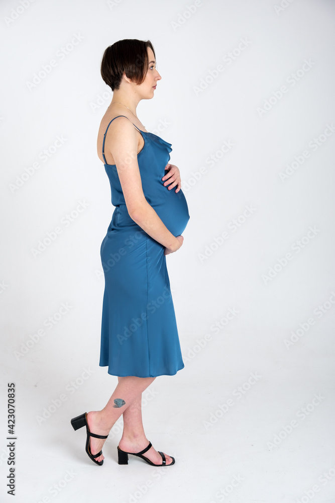 Studio portrait of young adult pregnant woman in blue dress on white gray background, happy pregnancy concept Studio portrait of young adult pregnant woman in blue dress on white gray background, happy pregnancy concept