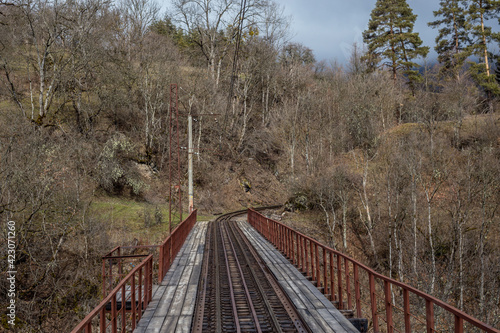 A single-track railway bridge in the woods turns a corner. Spring landscape in the mountains of Georgia.