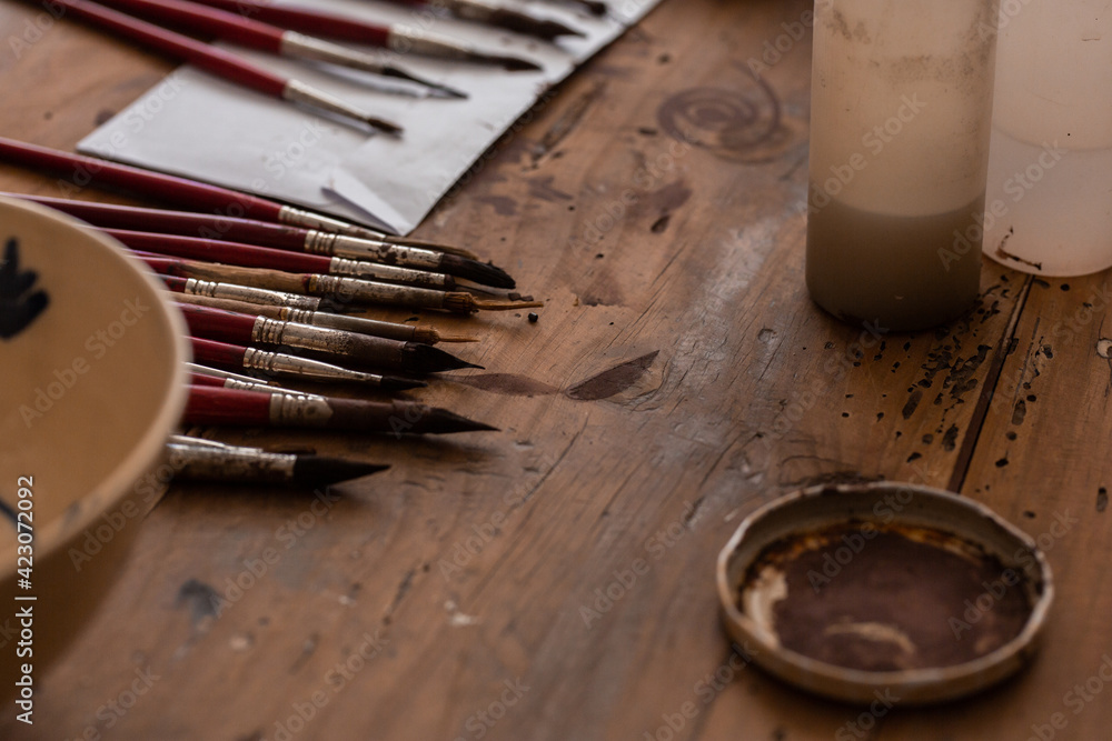 From above of various brushes near painted ceramic plate on wooden table in workshop From above of various brushes near painted ceramic plate on wooden table in workshop