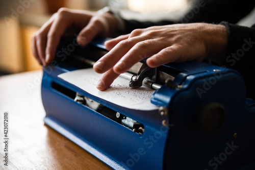 Crop anonymous visually impaired male typing on typewriter with tactile writing system  at home