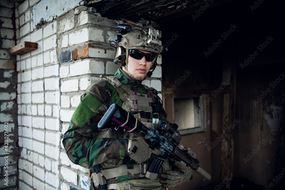 Fototapeta premium Military man with assault rifle standing inside building, he is ready for combat