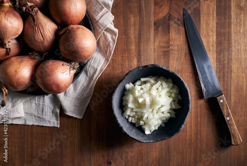 Top view of rustic bowl with pieces of cut onion placed near knife on lumber table in kitchen photo