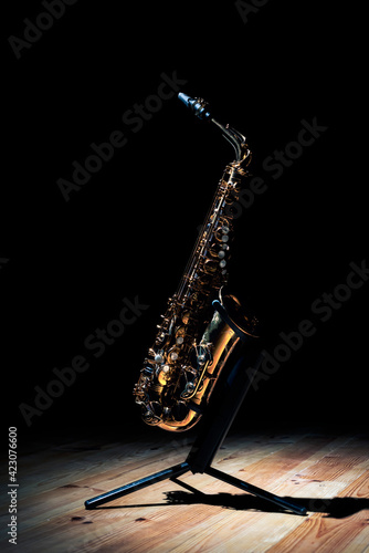 Shiny golden tenor saxophone on stand placed on wooden stage against black background photo