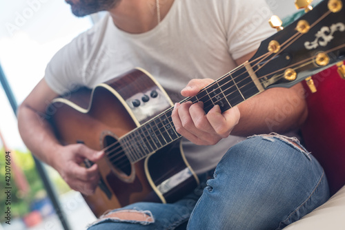 Crop of unrecognizable bearded male musician playing acoustic guitar on sofa