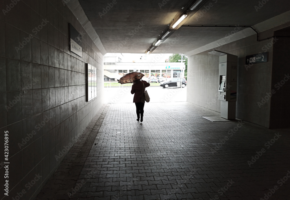 Cracow, Poland: A girl walking inside a tunnel subway of train station with umbrella in an urban city
