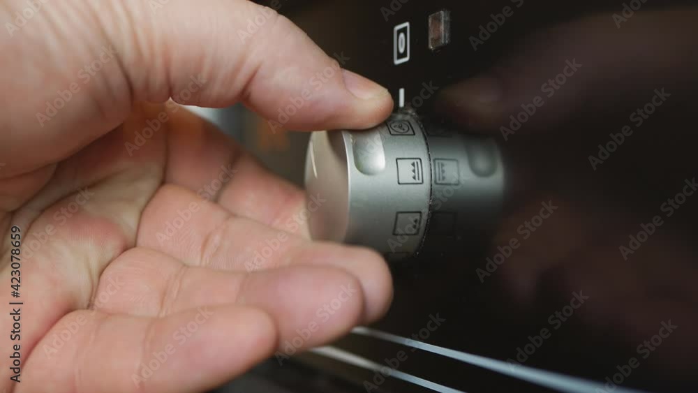 Manual activation of temperature switch of oven electric stove in kitchen.the hand turns the handle of the electric stove. Manual activation of temperature switch of oven electric stove in kitchen.the hand turns the handle of the electric stove.