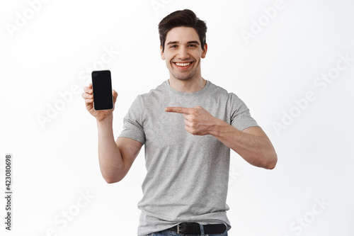 Portrait of smiling adult man pointing and showing empty smartphone screen, showing blank display phone, recommending app or online store, white background