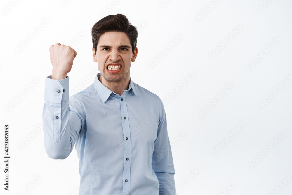 Angry office worker shaking fist in threaten, look outraged and pissed-off, standing frustrated against white background Angry office worker shaking fist in threaten, look outraged and pissed-off, standing frustrated against white background