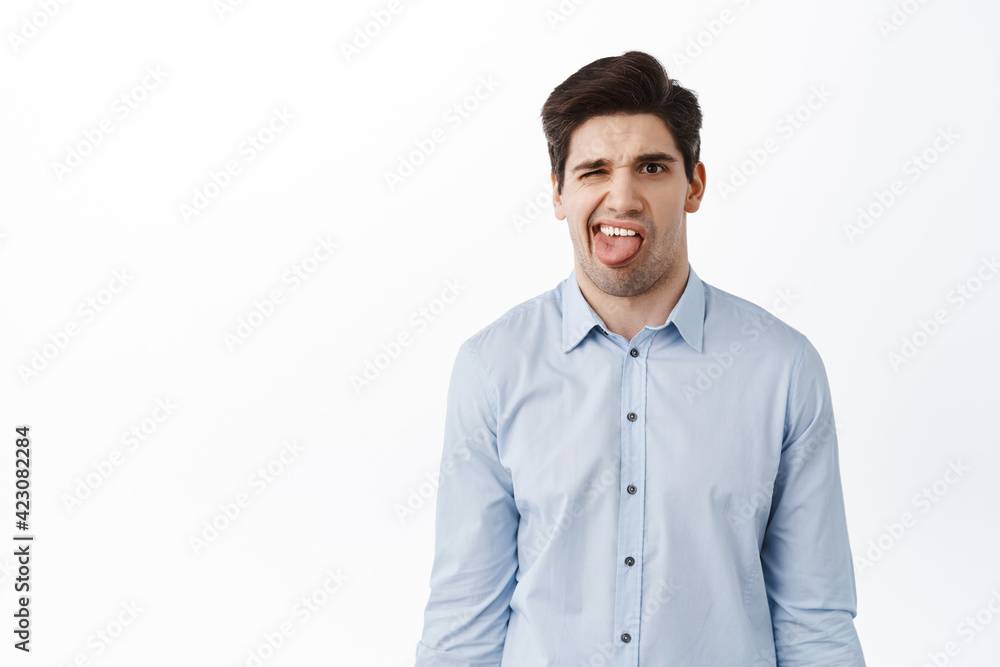 Confused and disgusted young man, office guy showing tongue and complain on bad tasty, something awful, dislike, white background