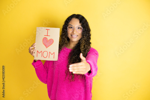 Beautiful woman celebrating mothers day holding poster love mom message smiling friendly offering handshake as greeting and welcoming