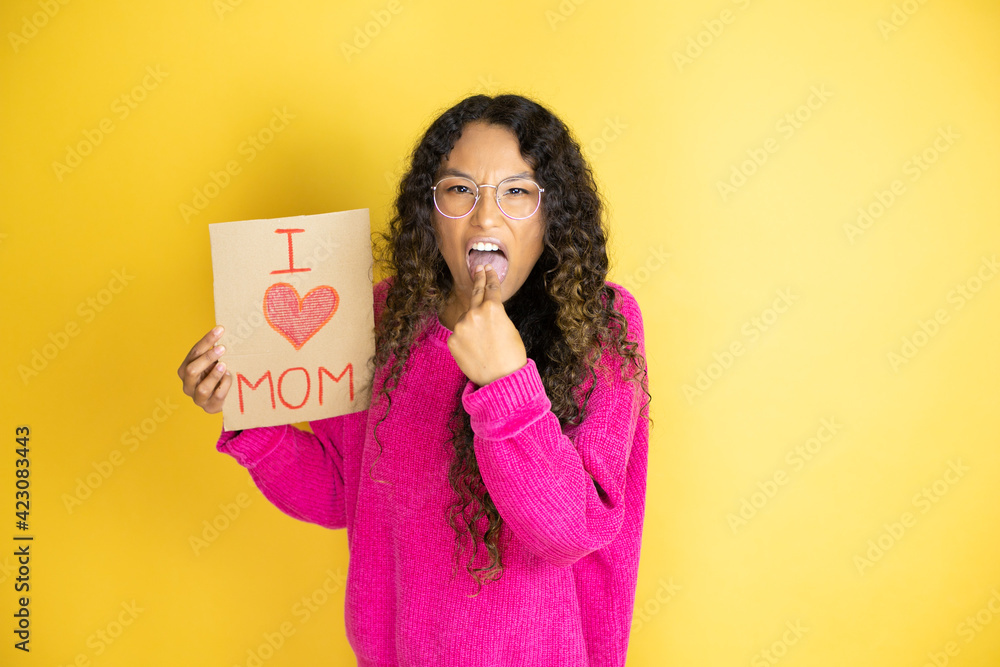 Beautiful woman celebrating mothers day holding poster love mom message disgusted with her hand inside her mouth Beautiful woman celebrating mothers day holding poster love mom message disgusted with her hand inside her mouth