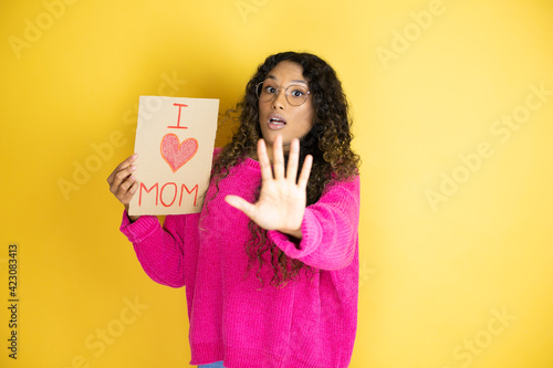 Beautiful woman celebrating mothers day holding poster love mom message afraid and terrified with fear expression stop gesture with hands, shouting in shock. Panic concept.
