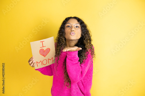 Beautiful woman celebrating mothers day holding poster love mom message looking at the camera blowing a kiss with hand on air being lovely and sexy. Love expression.