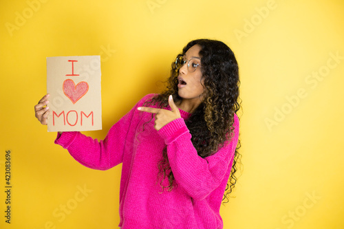 Beautiful woman celebrating mothers day holding poster love mom message amazed and pointing with hand and finger