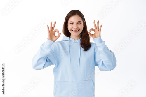 Young girl student say yes, showing okay signs in approval, accept something good, praise choice. Woman show OK gesture as like and compliment thing, standing over white background