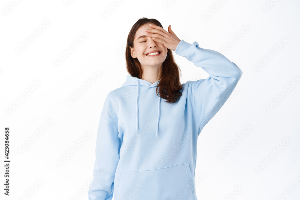 Image of happy and carefree teen girl smiling and touching face with hand, close eyes joyfully, feeling relaxed and upbeat, standing against white background Image of happy and carefree teen girl smiling and touching face with hand, close eyes joyfully, feeling relaxed and upbeat, standing against white background