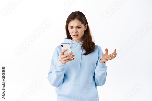 Image of a confused young beautiful woman posing isolated over white wall background using mobile phone
